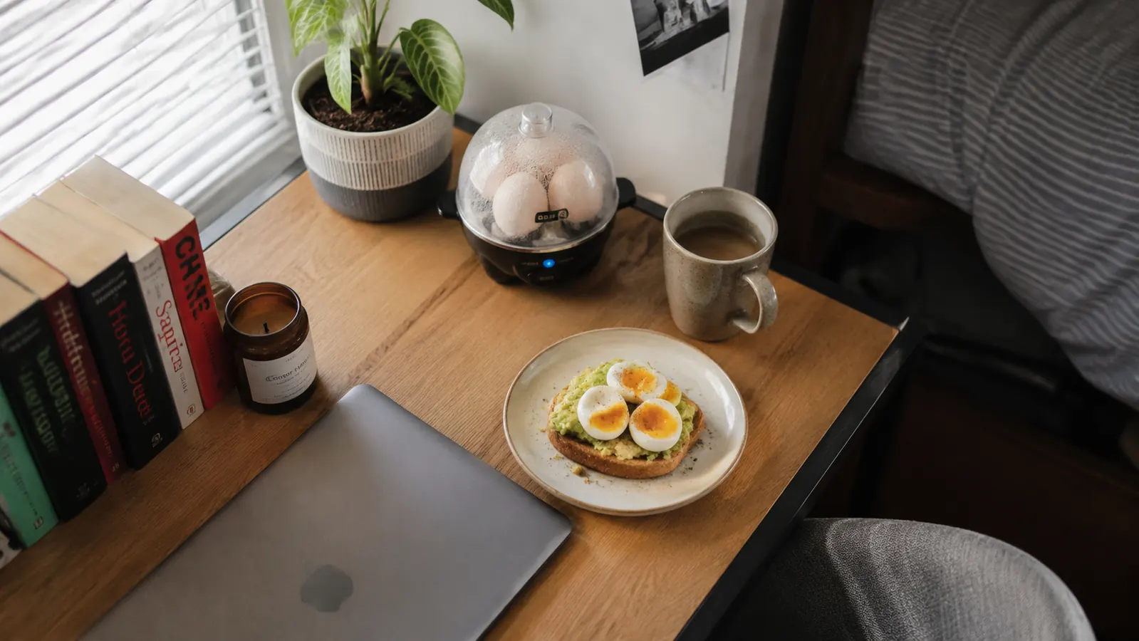 Top-down view of a dorm room desk with a Dash egg cooker, a mug, and a laptop, showing how small the footprint is
