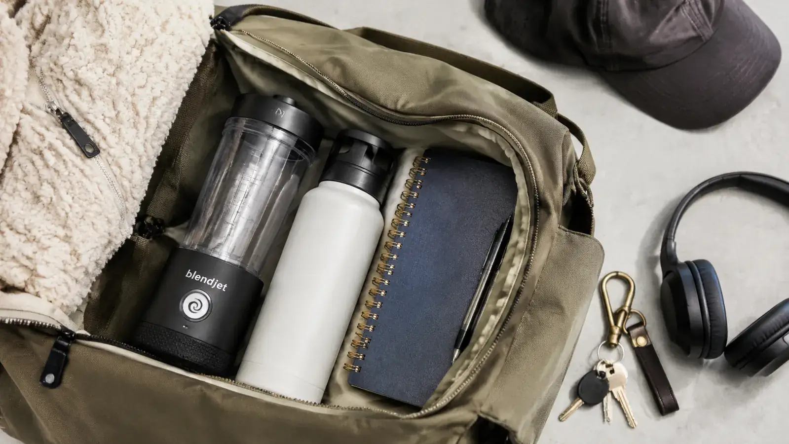 Magic Bullet blender cup and base packed into a travel bag alongside a water bottle and notebook
