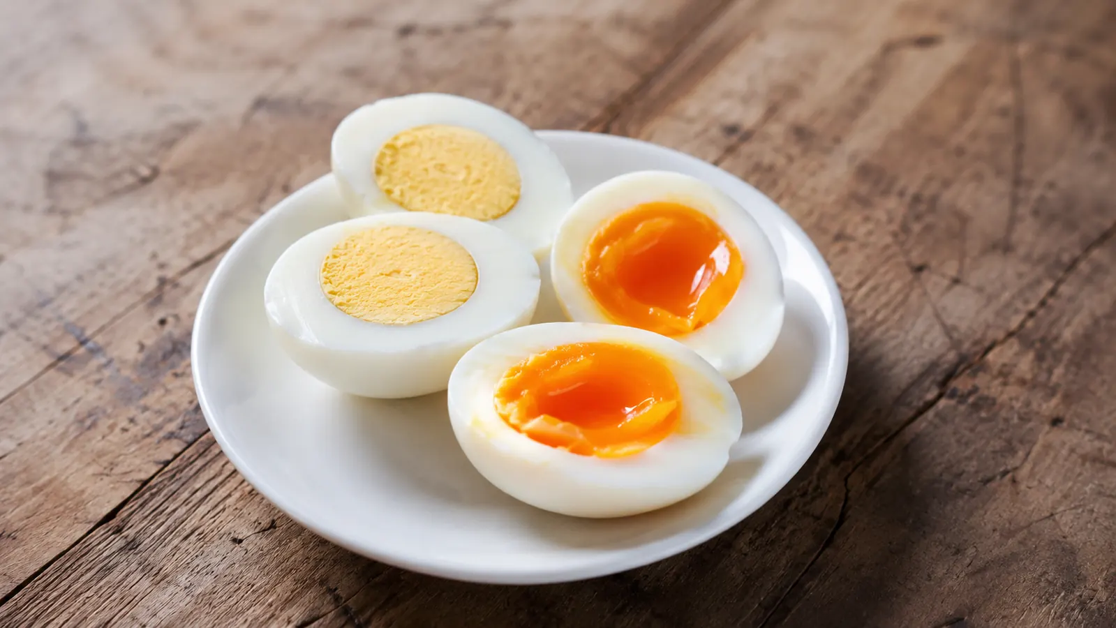 Perfectly cooked hard-boiled and soft-boiled eggs peeled and sitting on a small plate