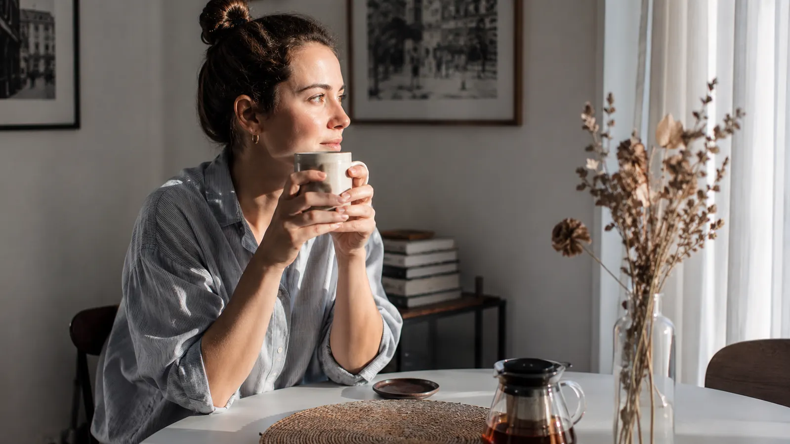 Person sitting at a small apartment dining table with a cup of tea, morning light, relaxed