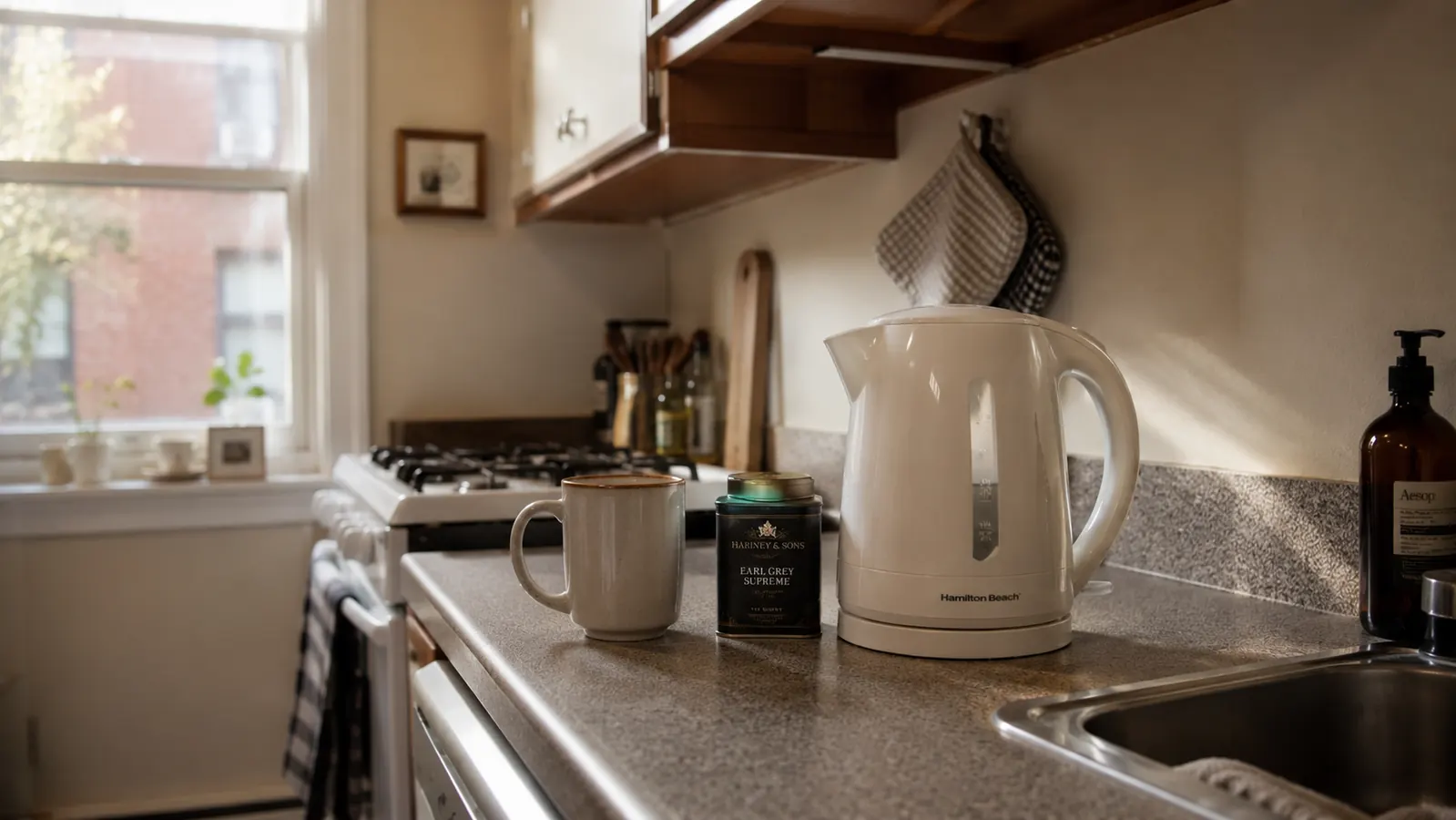 Hamilton Beach electric kettle sitting on a compact apartment kitchen counter beside a mug and tea tin