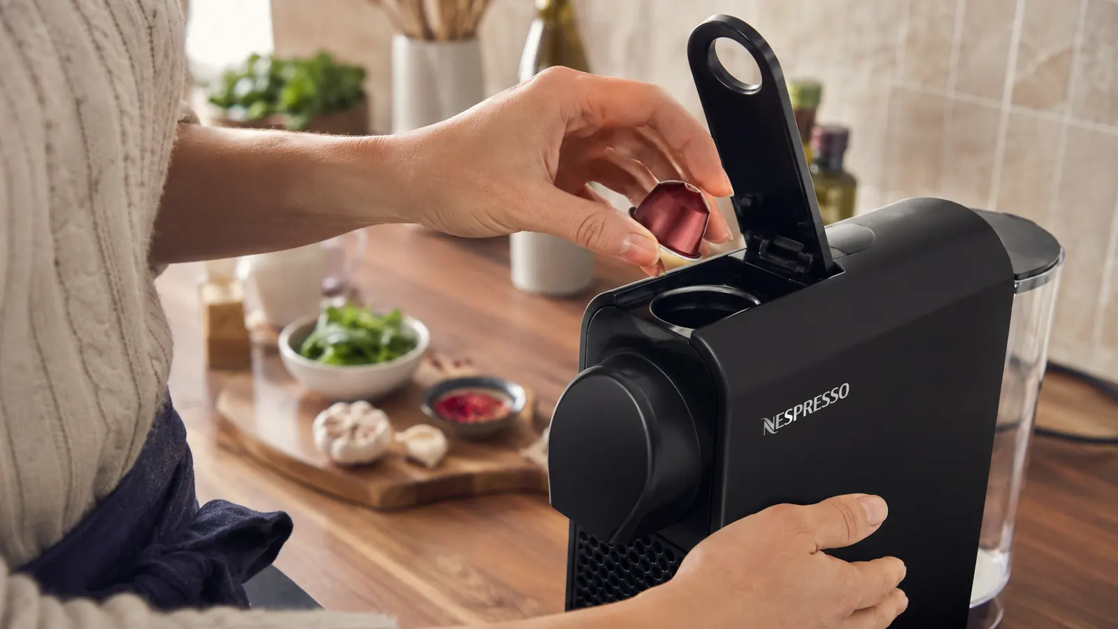 Hand placing a Nespresso capsule into the Nespresso Essenza Mini on a kitchen counter