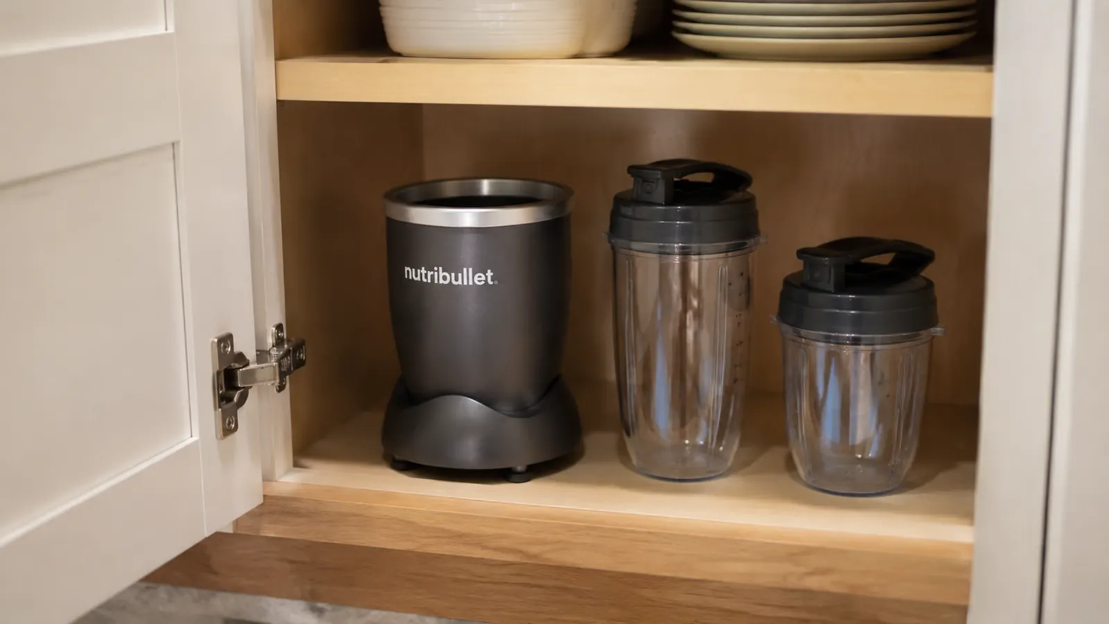 Compact personal blender base and two cups stored neatly in a kitchen cabinet, taking up minimal shelf space