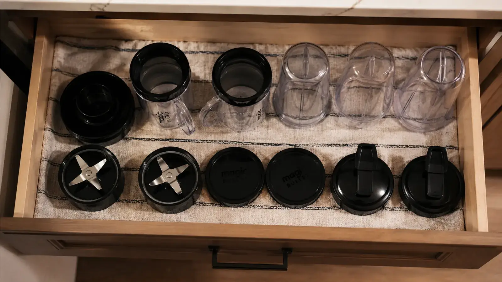 Overhead view of a small kitchen drawer with the Magic Bullet 11-piece set stored flat and organized