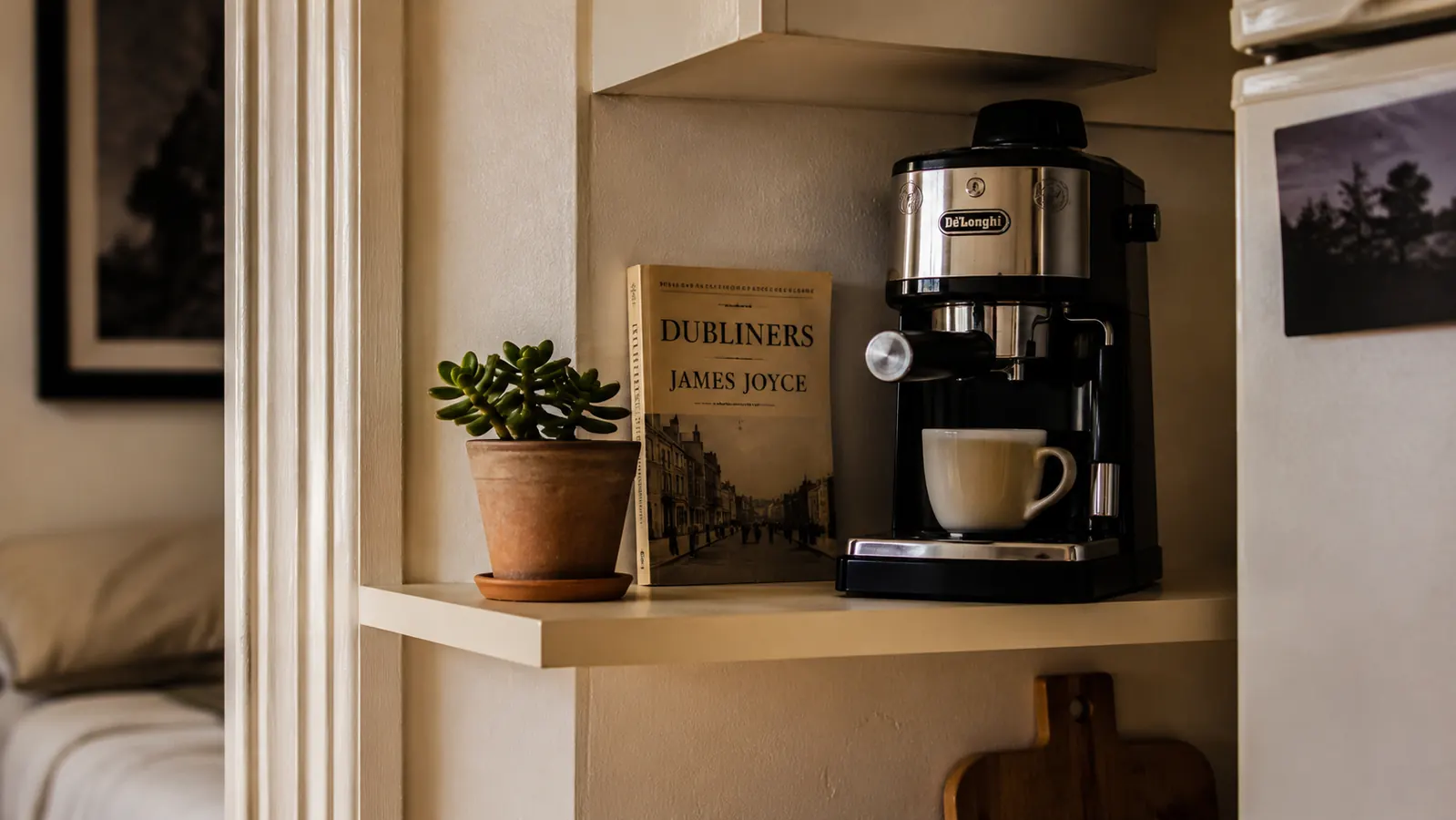 Espresso machine sitting beside a small plant and a book on a tidy apartment kitchen shelf